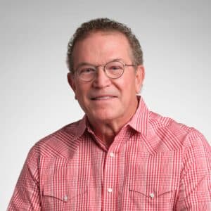 Portrait of a middle-aged man wearing glasses and a red checkered button-down shirt, smiling against a neutral studio background.