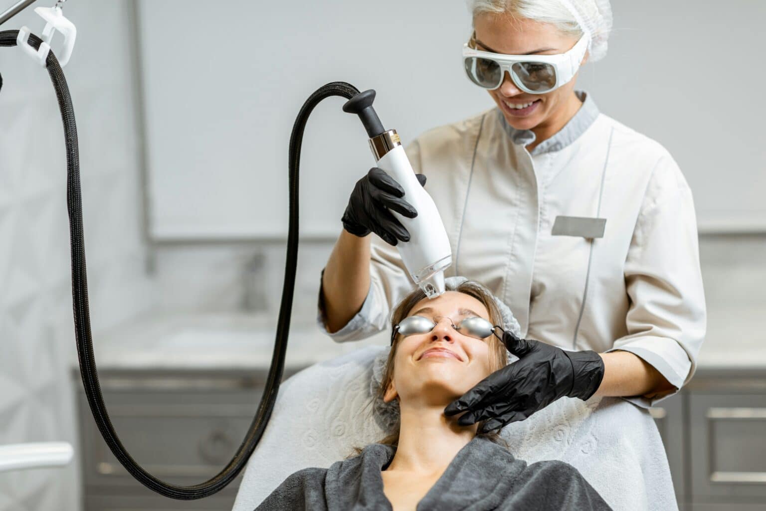 Aesthetic provider performing a laser facial treatment on a smiling patient wearing protective eyewear, representing BBL or Moxi therapy.