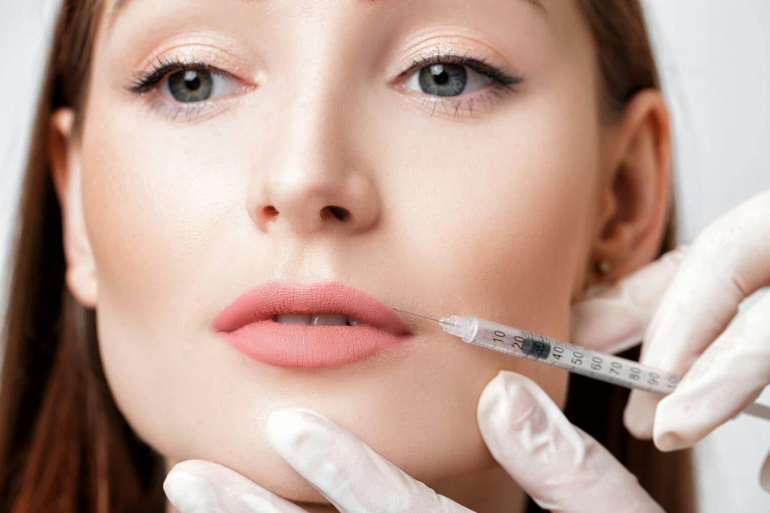 Clinician administering a dermal filler injection to the lower lip during a cosmetic lip enhancement treatment.
