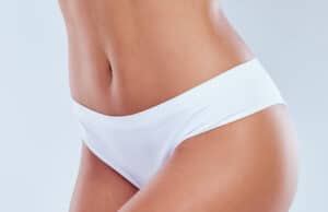 Close-up of a woman’s midsection in white underwear, highlighting a smooth lower abdomen and inner thigh area.