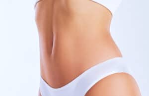 Close-up of a woman’s toned waist and lower abdomen in white underwear, highlighting smooth, contoured skin.