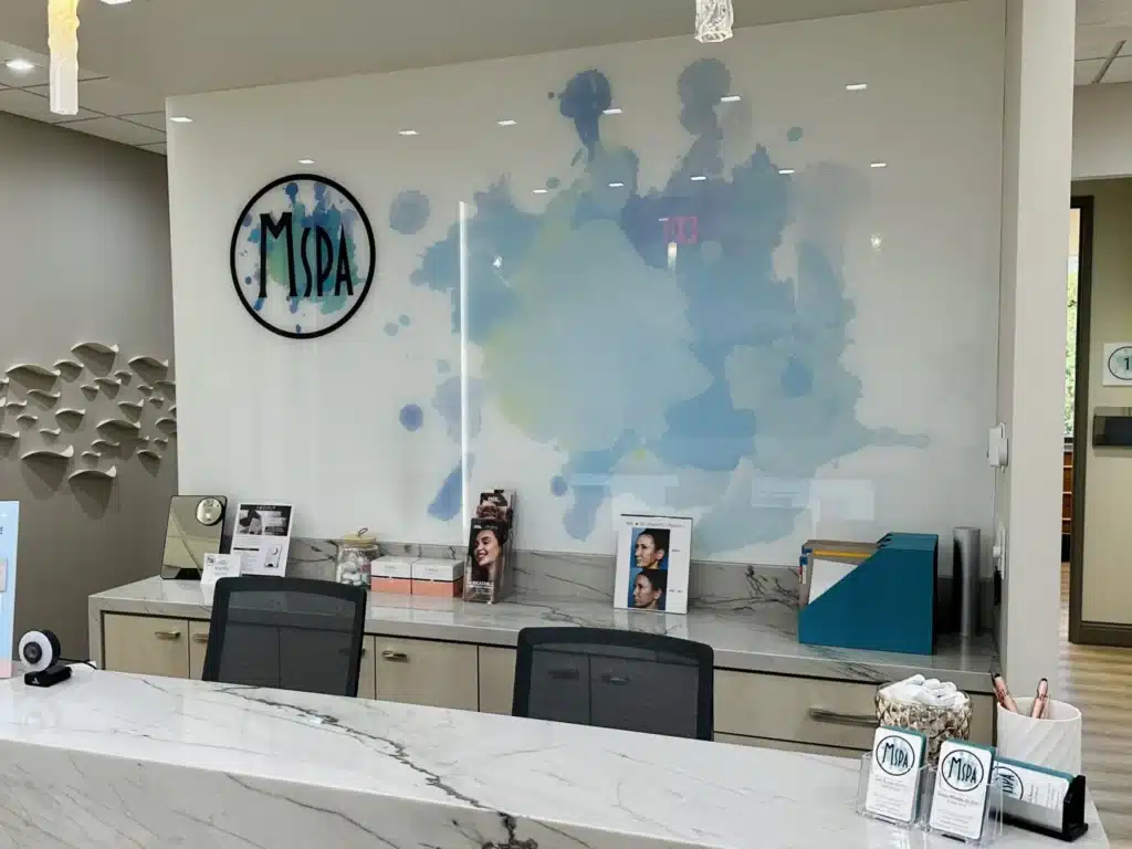 MSPA reception area with marble desk, watercolor accent wall, and framed skincare displays.