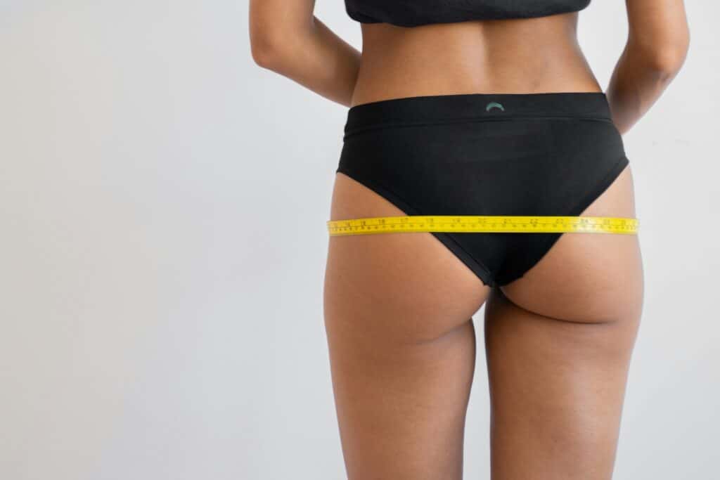 Woman in black bikini measuring hips showing weight loss results
